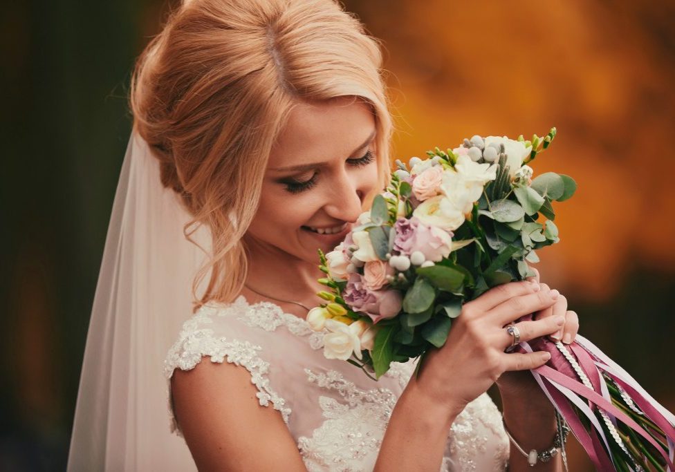 Beautiful bride smelling wedding bouquet in autumn park close up on wedding day.